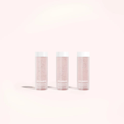 Three Solawave Skin Therapy Activating Serum Refill bottles stand on a light pink background. Transparent with white caps, revealing the pink liquid inside and shadows beneath, they perfectly complement the Solawave Wand treatment and its anti-aging ingredients.