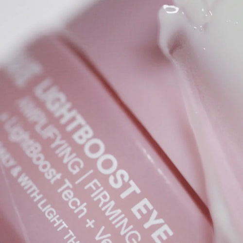 Close-up of a soft pink cosmetic container with white text partially visible: LightBoost Eye Amplifying | Firming. The LightBoost Eye Cream by Solawave is infused with vegan collagen, suggesting advanced skincare technology.