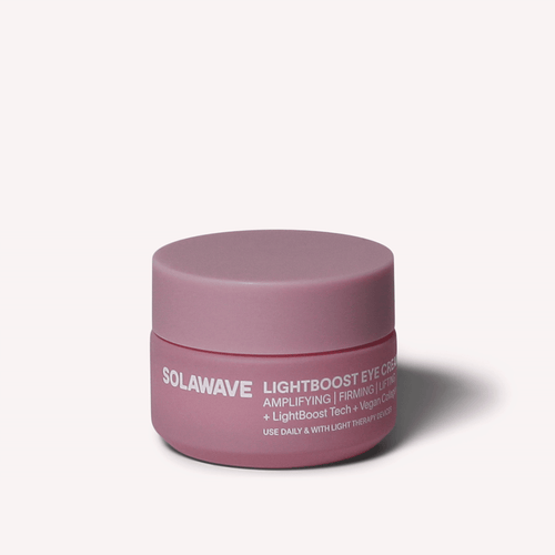 A pink round jar labeled Solawave LightBoost Eye Cream boasts benefits like amplifying, firming, and lifting with LightBoost Tech and vegan collagen, enhanced by light therapy. It features a matching lid against a soothing pale pink background.